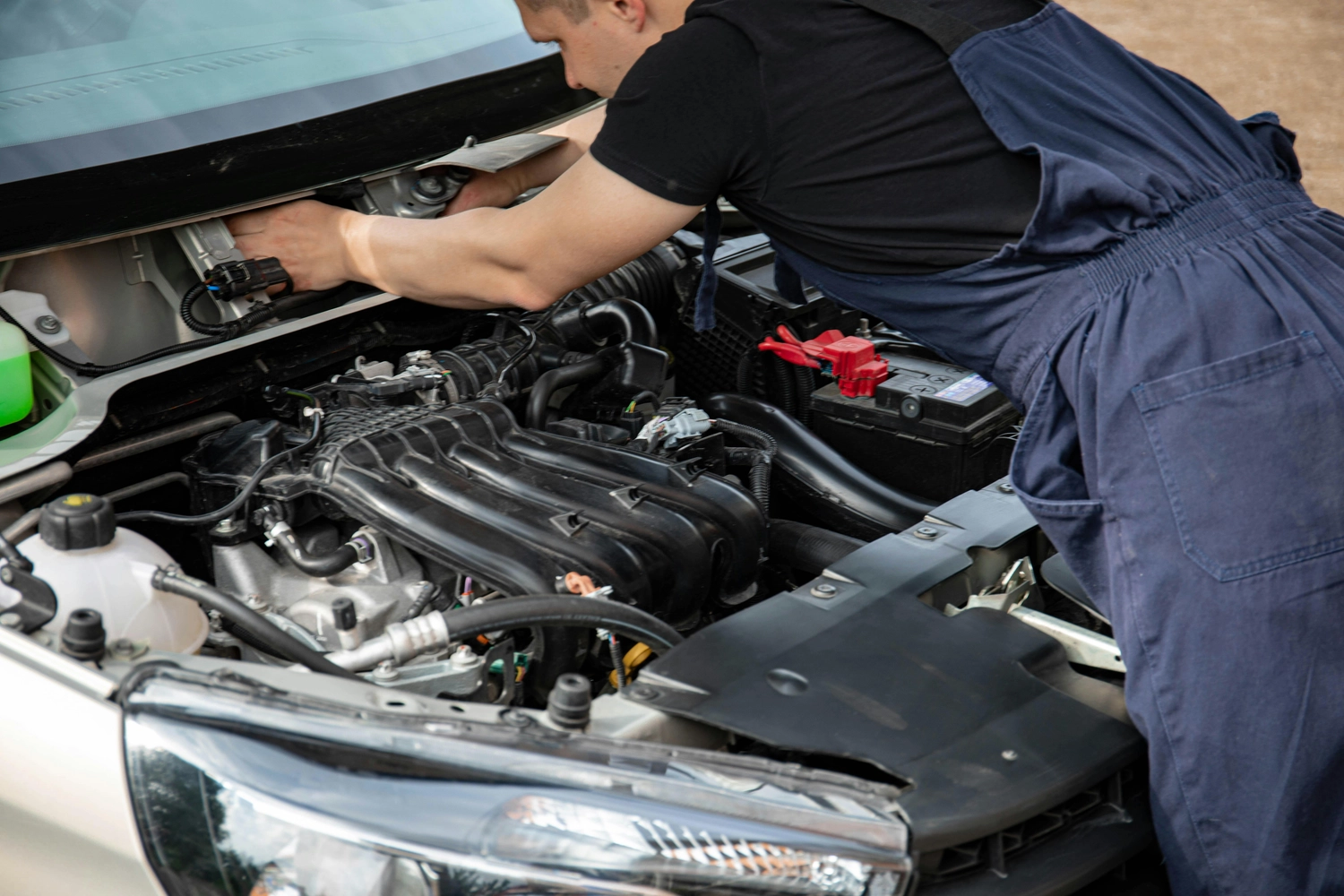 Mobiler Gasservice und Serviceleistung – Serviceleistungen rund um Wohnmobil und Wohnwagen – Mechaniker im blauen Overall, der bei geöffneter Motorhaube an einem Automotor arbeitet